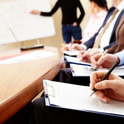 Close-up of businesspeople hands holding pens and papers near table at business seminar